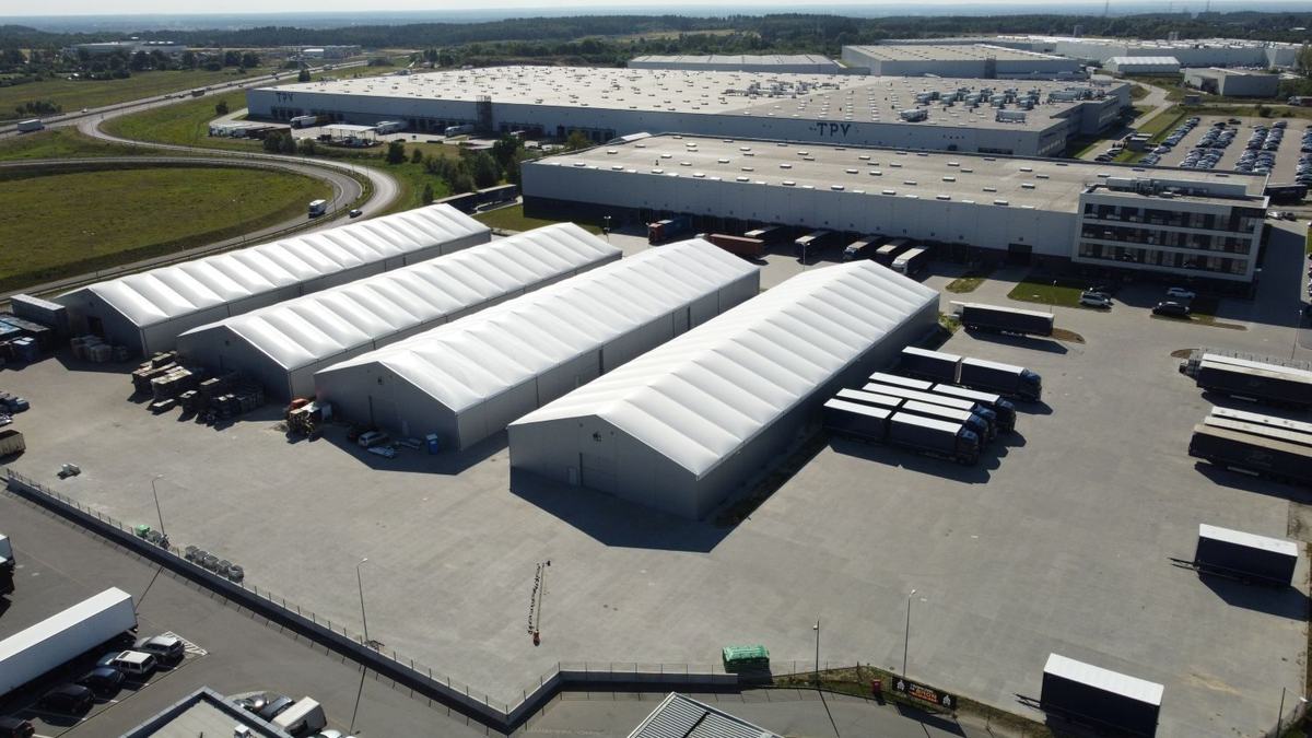 Cztery hale namiotowe obok magazynów z rampami w parku logistycznym, widok z góry